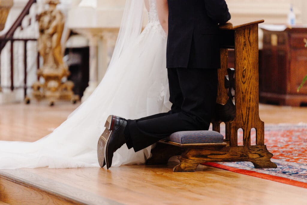 bride and groom kneeling on a kneeler at their nuptial mass. Image focuses on the kneeler.