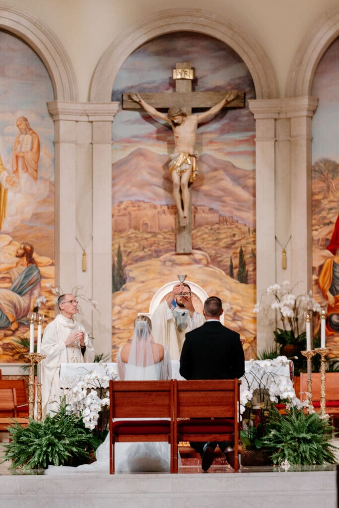 bride and groom kneeling in front of the altar during consecration. the Priest holds the host